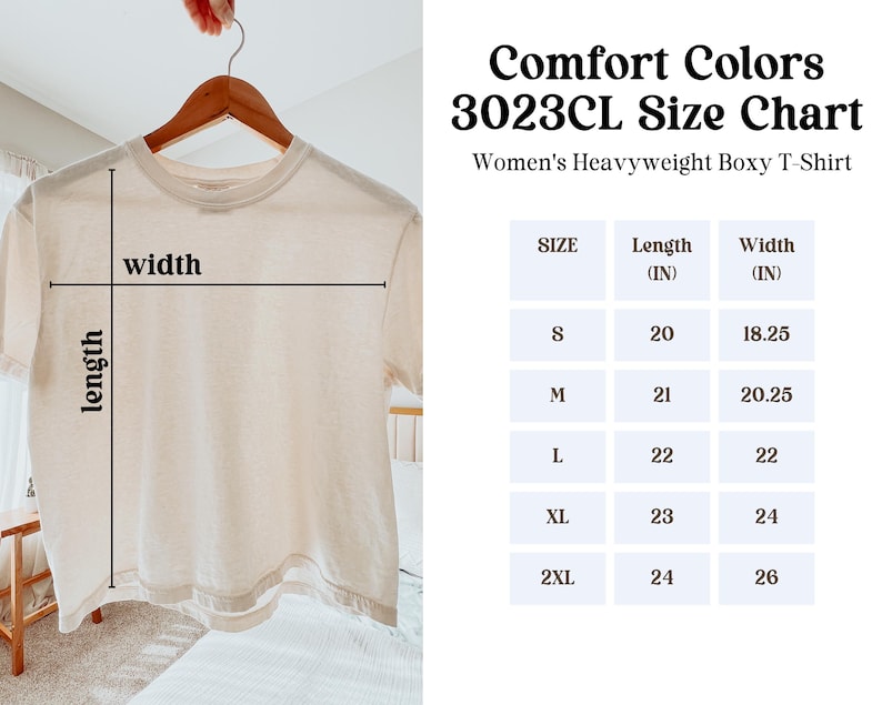 May include: A cream-colored, heavyweight boxy t-shirt hangs on a wooden hanger. The image includes a size chart with measurements in inches for sizes S to 2XL. The text on the chart reads "Comfort Colors 3023CL Size Chart" and "Women's Heavyweight Boxy T-Shirt."