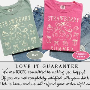 May include: Two t-shirts, one in a muted green and the other in bright pink, both featuring a strawberry-themed graphic with the words "STRAWBERRY SUMMER". The shirts are paired with denim shorts. The green shirt is labeled "BAY" and the pink shirt is labeled "CRUNCH BERRY".