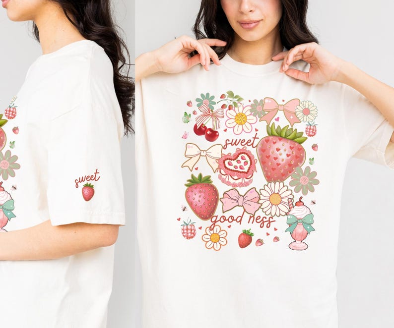 Op de afbeelding: Cr&egrave;mekleurig T-shirt met een aardbeienthema. Het ontwerp bevat aardbeien, strikken, bloemen en de woorden "sweet good ness". Een kleinere versie van het ontwerp staat op de mouw.