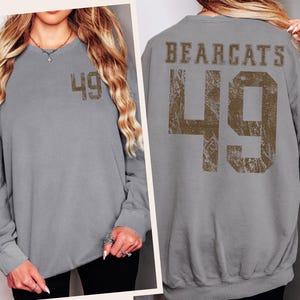 May include: A gray sweatshirt with the number 49 printed on the front and back. The back of the sweatshirt also features the word "BEARCATS" above the number. The number and text are in a distressed, brown font.