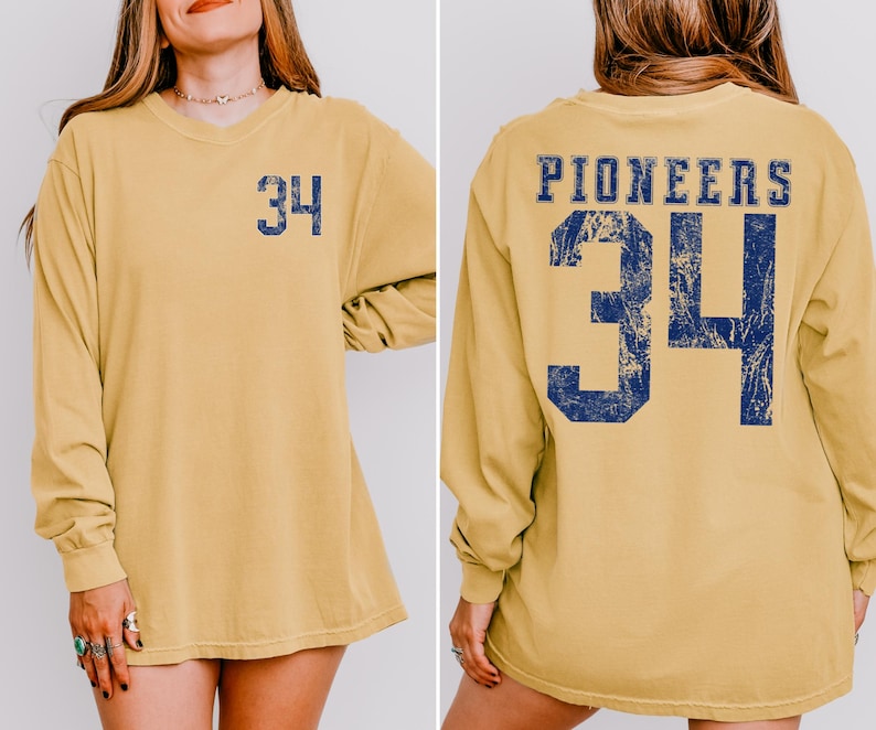 May include: Mustard yellow long-sleeve shirt with the number 34 in navy blue on the front and back. The word "PIONEERS" is printed above the number on the back. The shirt has a relaxed fit and a crew neck.