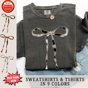 May include: A gray sweatshirt with a leopard print bow on the front. The sweatshirt is available in 9 colors. "Pick Your Bow" is written on a red starburst sticker.