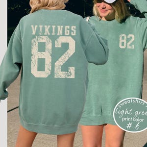 May include: Light green sweatshirt with the word "VIKINGS" and the number "82" printed on the back in a distressed, off-white font. The front of the sweatshirt also features the number "82". The text "sweatshirt in light green print color #6" is in a circle.