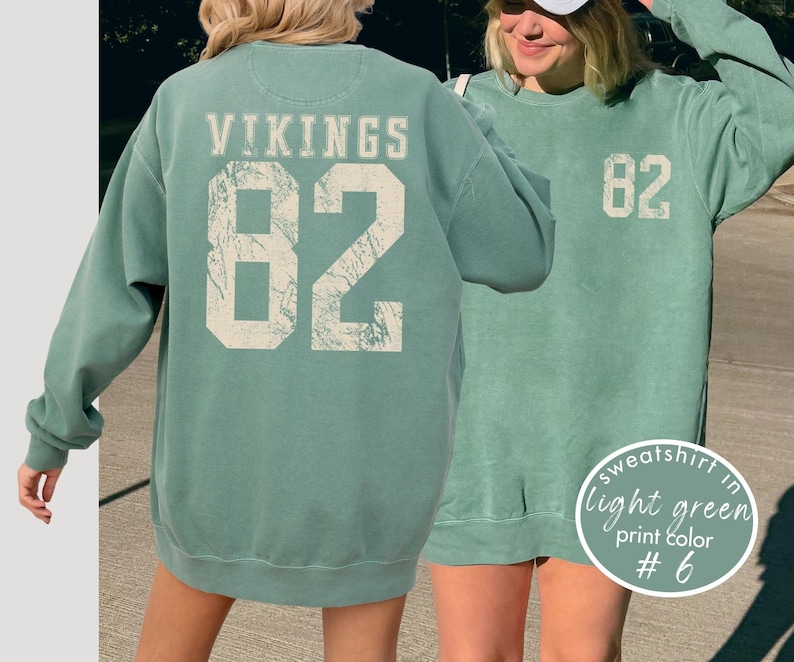 May include: Light green sweatshirt with the word "VIKINGS" and the number "82" printed on the back in a distressed, off-white font. The front of the sweatshirt also features the number "82". The text "sweatshirt in light green print color #6" is in a circle.