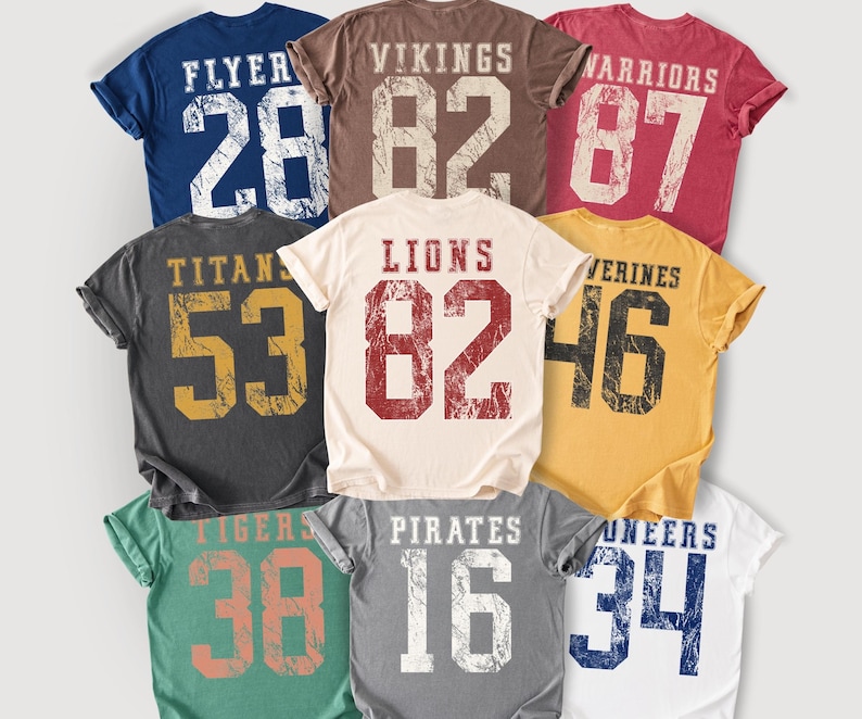 May include: A collection of vintage-style t-shirts in various colors, each featuring a team name and number. The shirts include "FLYER 28", "VIKINGS 82", "WARRIORS 87", "TITANS 53", "LIONS 82", "WOLVERINES 46", "TIGERS 38", "PIRATES 16", and "PIONEERS 34".