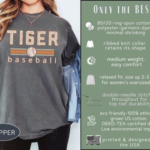 May include: Pepper-colored t-shirt with "TIGER baseball" text in orange and white, featuring a baseball graphic. The shirt is made of ring-spun cotton and polyester, with a relaxed fit and double-needle stitching. Printed and designed in the USA.