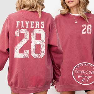 May include: Crimson-colored sweatshirt with the word "FLYERS" and the number "28" printed in white on the back. The front of the sweatshirt also features the number "28" in white. The sweatshirt is a crew neck style.