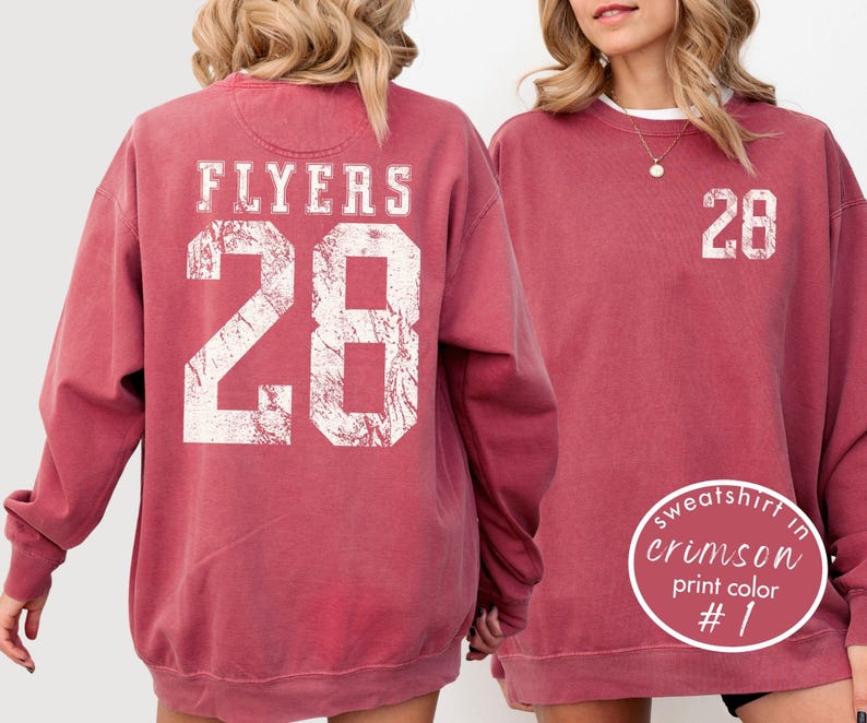 May include: Crimson-colored sweatshirt with the word "FLYERS" and the number "28" printed in white on the back. The front of the sweatshirt also features the number "28" in white. The sweatshirt is a crew neck style.