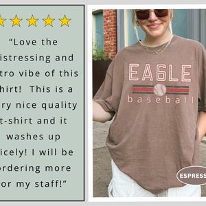 May include: Espresso-colored t-shirt with the word "EAGLE" in a distressed, retro style, with a baseball graphic. The word "baseball" is below the graphic. The shirt has a vintage look.
