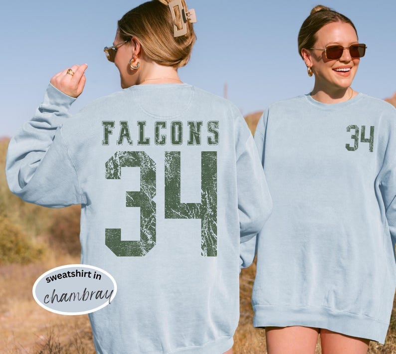 May include: Light blue sweatshirt with the word "FALCONS" and the number "34" printed in distressed green. The sweatshirt is a casual style, perfect for sports fans.