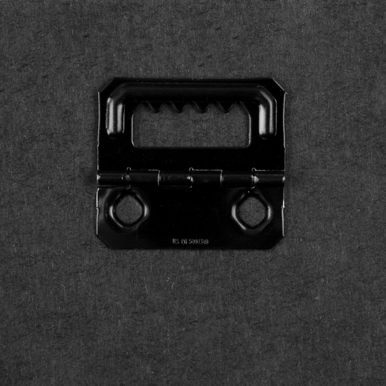 May include: Black metal picture hanging hardware with two screw holes and a sawtooth hanger. The hardware has the text "RS. DR 50001548" printed on the bottom.