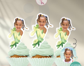 May include: Cupcakes with custom face toppers featuring a young girl dressed as a princess. The toppers are placed on cupcakes with light green frosting in white cupcake liners. The text "CUSTOM FACE TOPPER" is visible.