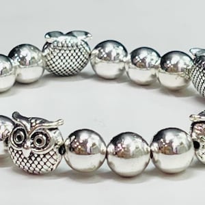 Puede incluir: Un brazalete de plata con abalorios de búho y cuentas redondas.