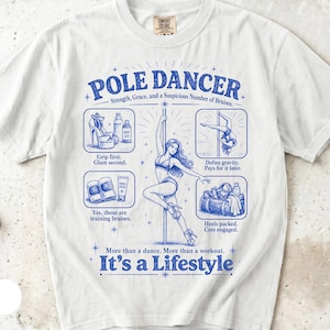 以下が含まれることがあります： POLE DANCER, Strength, Grace, and a Suspicious Number of Bruisesというテキストが青色でプリントされた白いTシャツ。ポールダンスをする人物、プラットフォームヒール、グリップ剤、ジムバッグなどのイラストと説明文がデザインされています。