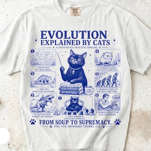 Peut inclure: Un t-shirt blanc à manches courtes avec une impression graphique bleue intitulée EVOLUTION EXPLAINED BY CATS. Le design montre une chronologie en sept étapes avec un chat en professeur, incluant le texte FROM SOUP TO SUPREMACY et diverses légendes.
