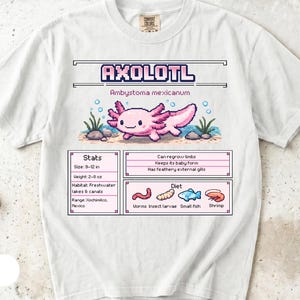 Może przedstawiać: Biały t-shirt z grafiką pixel art przedstawiającą różowego aksolotla. Wzór zawiera napis AXOLOTL, Ambystoma mexicanum oraz tabelę statystyk z wymiarami 23-30 cm, wagą 57-227 g, siedliskiem oraz sekcją diety z ikonami przedstawiającymi pokarm.