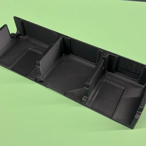 May include: Black plastic organizer with four compartments. The organizer has a textured surface and is designed to hold small items.