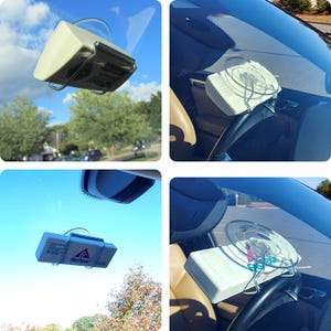 Puede incluir: Un soporte de parabrisas de coche blanco con una ventosa y un clip de metal. El soporte sostiene un dispositivo blanco con el texto "FastTrac" en &eacute;l.