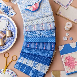 May include: A collection of blue and white patterned fabrics, buttons, and decorative elements. The fabrics feature floral, polka dot, and elephant designs. A bird-shaped applique and gold scissors are also present, suggesting a sewing or craft theme.