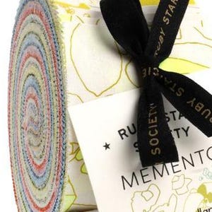Peut inclure: Un paquet roulé de bandes de tissu de différentes couleurs, noué avec un ruban noir. Le rouleau de tissu présente un motif floral. Une étiquette avec le texte "MEMENTO" et "carolyn friedlander" est attachée.