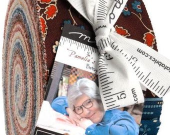 May include: A jelly roll of fabric strips featuring dark brown, teal, and orange floral patterns. The roll is tied with a white ribbon printed with a ruler design and the text moda fabrics. A tag displays the text moda FABRICS + SUPPLIES.