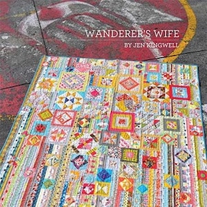 May include: A vibrant patchwork quilt with a mix of patterned squares and strips in a variety of colours. The quilt has a blue border and the text "Wanderer's Wife" by Jen Kingwell.