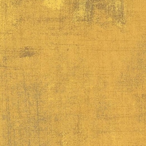 May include: Textured fabric in golden yellow and grey. The fabric has a distressed, aged look with brushstroke-like patterns. A ruler with inch measurements is along the bottom edge. The fabric is from Moda Fabrics.