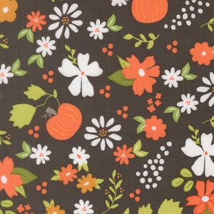 May include: Dark brown fabric with a repeating pattern of orange pumpkins, white and orange flowers, green leaves, and small white dots. The fabric has a ruler along the bottom with the word "moda" printed on it.