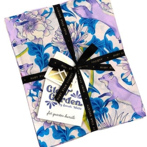 May include: A bundle of fabric featuring a floral and fox print in shades of blue, purple, and white. The fabric is tied with a black ribbon and a tag that reads "Glow Garden by Sarah Watts fat quarter bundle".