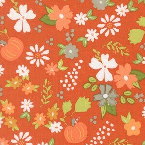 May include: Orange fabric with a repeating pattern of pumpkins, white and orange flowers, green leaves, and gray accents. The fabric has a ruler along the bottom with the word "moda" printed on it.