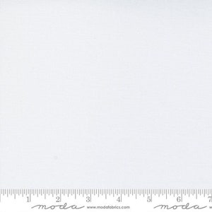 May include: A plain white fabric swatch with a ruler showing measurements in inches. The ruler has the word "moda" printed on it.