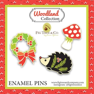 May include: Three enamel pins featuring a red and green holly wreath, a black and white hedgehog with green pine needles, and a red and white mushroom with white polka dots. The pins are part of the Woodland Collection by Fig Tree & Co.