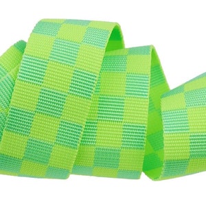 May include: A length of bright green and light green checkered ribbon, curled and layered against a white background. The ribbon has a woven texture and a repeating square pattern. The ribbon is likely used for crafting or gift wrapping.