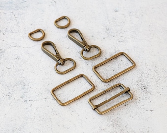 May include: A set of antique gold metal hardware for leather crafting projects. The set includes two swivel clasps, two D-rings, two rectangular buckles, and one rectangular buckle with a centre bar.