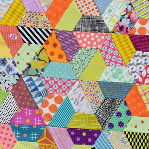 May include: Close-up of a patchwork quilt with a geometric pattern. The quilt is made of hexagonal fabric pieces in a vibrant array of colours and patterns, including polka dots, stripes, and floral designs.