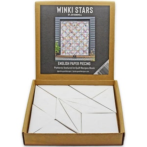 May include: An open cardboard box containing white paper piecing shapes. The box lid features the text "WINKI STARS" and "ENGLISH PAPER PIECING" with a colorful quilt image. The product is by Jen Kingwell.