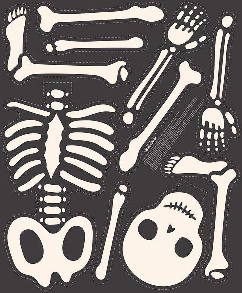 May include: A collection of cream-colored, die-cut skeleton pieces on a dark gray background. The set includes a skull, rib cage, limbs, hands, and feet, all with a stitched outline. The pieces are designed for Halloween or themed crafts.