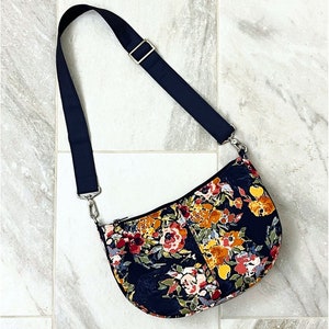 May include: A black floral half-moon shaped bag with a black adjustable shoulder strap. The bag measures approximately 8 inches high by 12 inches wide by 3 inches deep.  ATB-232 Emma Half Moon Bag