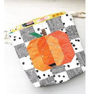 May include: A quilted drawstring bag project with a pumpkin design. The bag features a patchwork pattern in black and white, with an orange pumpkin applique. The finished size is 8" x 10" x 2". The text "Mini Pumpkin Drawstring Bag Project" is at the top.