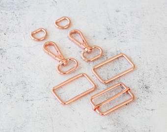 May include: A set of rose gold metal hardware for crafting, including two swivel clasps, two rectangular D-rings, and two smaller D-rings.