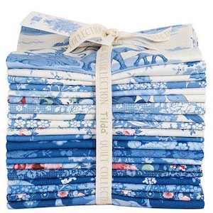 May include: A stack of blue and white patterned fabric squares tied with a cream ribbon. The fabric features floral, elephant, and landscape designs. The ribbon is printed with the words "COLLECTION Tilda QUILT COLLECTION".