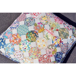 May include: A colorful patchwork pillow with a geometric design. The pillow is made of various fabrics with floral patterns in shades of red, blue, green, yellow, and white. The pillow is surrounded by a light gray fabric.