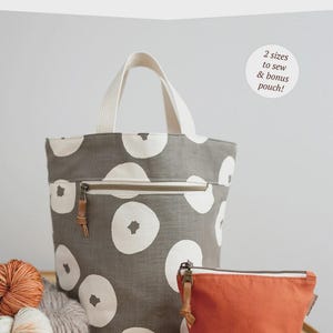 May include: A gray tote bag with white circular patterns and a matching orange zippered pouch. The tote has a white handle and a front zipper. The text "QUARRY TOTE" and "noodlehead" are visible.