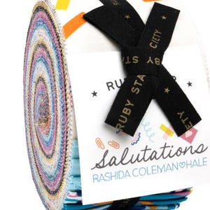 Peut inclure: Un rouleau de tissu coloré avec un fond blanc et des motifs géométriques. Le tissu est noué avec un ruban noir avec des lettres dorées qui lisent "Ruby Star Society". L'étiquette sur le rouleau de tissu indique "Salutations" et "Rashida Coleman Hale".