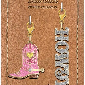 May include: Two zipper charms featuring a pink glitter cowboy boot with a yellow heart and a silver glitter charm with the word "HOMIE" in sparkly letters. The charms are packaged on a brown card with the text "Cathe Holden's sew cute zipper charms" and "mod fabrics + supplies".