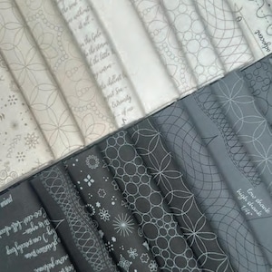 May include: A collection of folded fabric strips in shades of white, gray, and black. The fabric features printed white line patterns including geometric circles, floral motifs, and cursive text excerpts from Emily Dickinson poems and sewing terms.