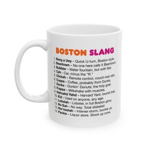 May include: White ceramic mug with a black and orange design. The mug features the text "Boston Slang" and a list of slang terms and their definitions.