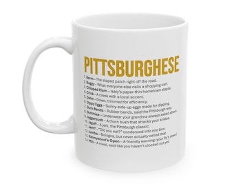 May include: White ceramic mug with a curved handle. The mug features the word "PITTSBURGHESE" in gold lettering, along with a list of definitions. The mug is a humorous gift idea.