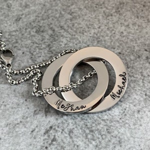 May include: A silver necklace with two interlocking circles. The circles are engraved with the names "Meghan" and "Michael".