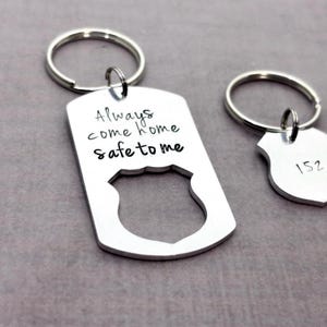 Two silver colored aluminum keychains with a police badge design. The larger keychain has the text 'Always come home safe to me' hand stamped on it. The smaller keychain is customizable.